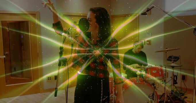 Singing woman red-plaid shirt leaning into pop mic, studio drummer playing red kit, overlay pulsing