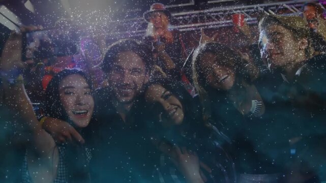 Five friends huddling at music gig, raising phone to capture or share shot, causing flash and glitte