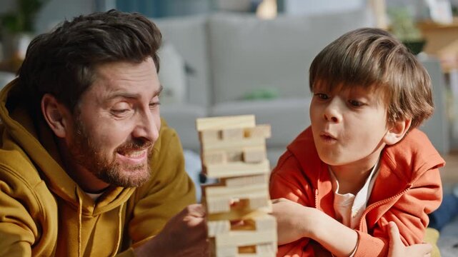 Father child competing jenga lying floor together closeup. Smiling man son