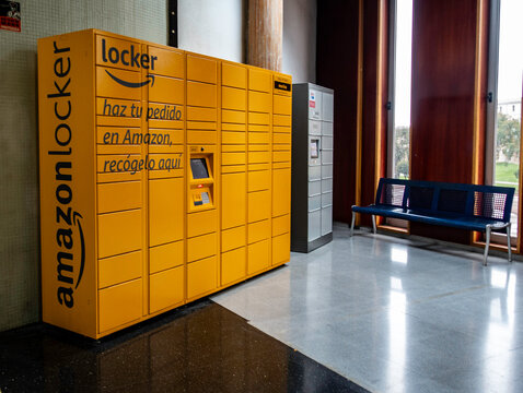 Yellow Amazon Hub Locker at Cartagena Bus Station, Spain, situated in a waiting area with a blue metal bench and natural light from large windows.