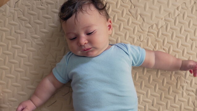 Baby lying on soft mat, arms outstretched, looking to the side, relaxed posture, early exploration, quiet observation, feeling safe and comfortable in a nurturing home setting