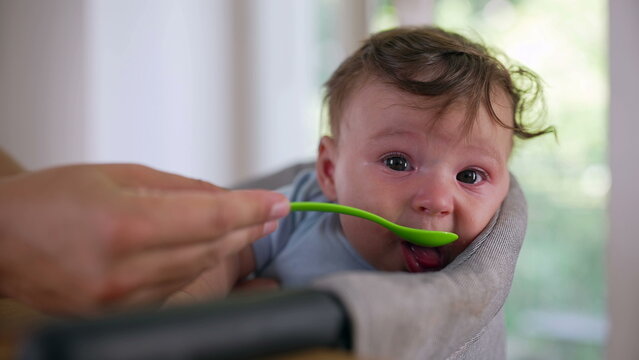 Baby reacting with teary eyes while being fed, resisting spoonful of food, showing discomfort, strong emotional response, early childhood feeding challenge