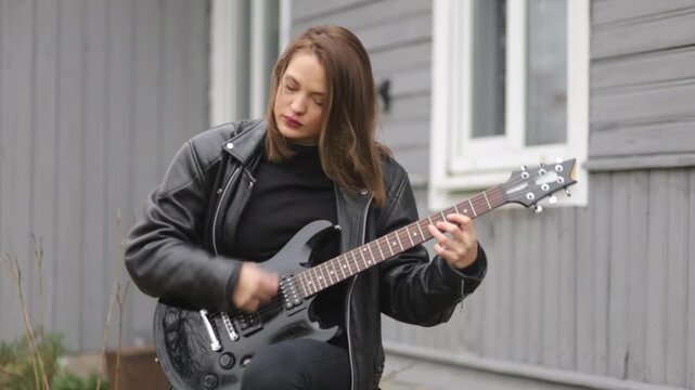 female rock musician in a leather jacket plays an electric guitar with an amplifier