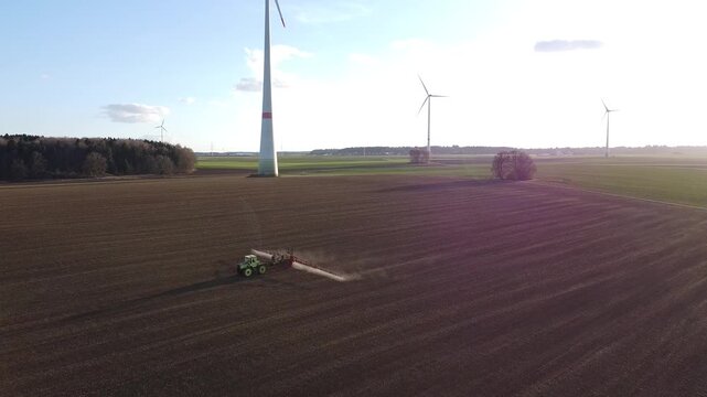 Aerial view of tractor spraying farmland with wind turbines at sunset &ndash; renewable energy concept