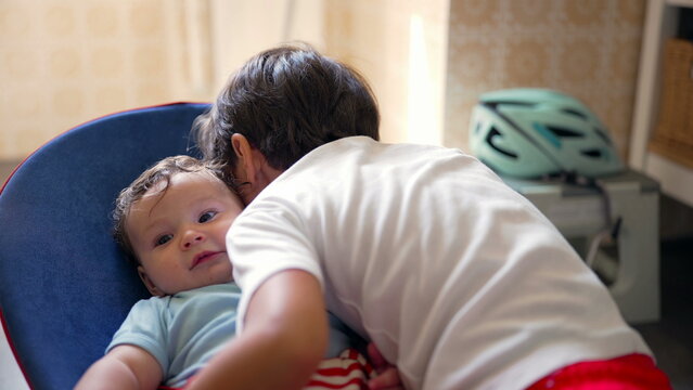 Young boy leaning in to hug baby in bouncer, warm sibling affection, gentle embrace, early childhood bonding, loving family relationship, emotional connection