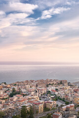 Obraz premium Vertical view of Tropea in Calabria, Italy, with coastal town buildings below a pastel sky and overlooking the sea.