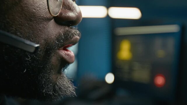 Side view close up shot of unrecognizable Black man working as police dispatcher and speaking into headset while answering calls with focus on lips moving at night