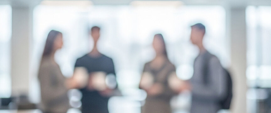 A group of four blurred individuals chatting in a modern office environment, conveying a sense of teamwork and collaboration in a professional setting.