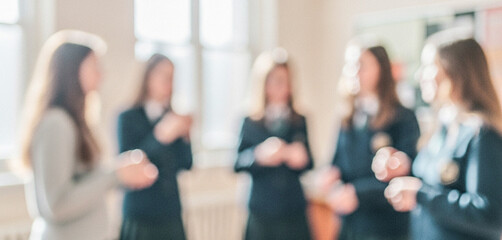 Fototapeta premium A group of students wearing uniforms engaged in a conversation in a bright classroom with blurred backgrounds, portraying a sense of camaraderie and youth.