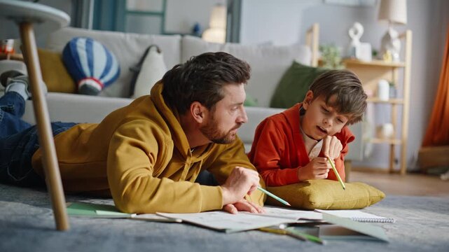 Father teaching schoolboy homework solving tasks together lying floor closeup.