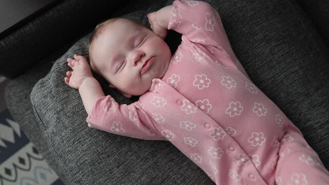 Baby girl in pink romper lying on her back, stretching after sleep and touching her face with small hands