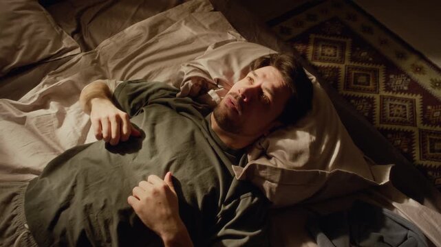 High angle shot of troubled adult man lying down on bed struggling with anxious thoughts while getting up in morning