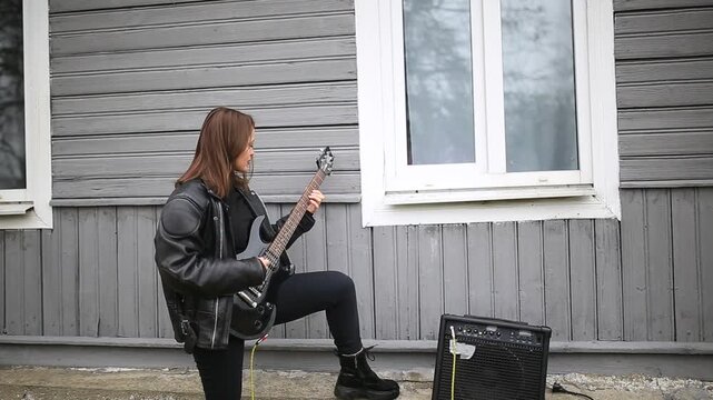 female rock musician in a leather jacket plays an electric guitar with an amplifier