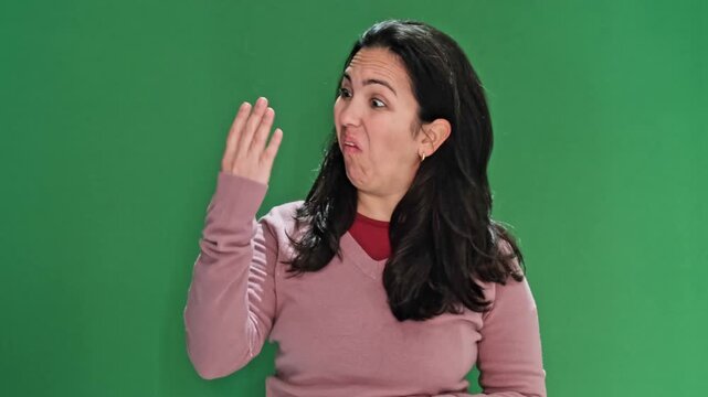 Middle-aged hispanic woman gesturing disgust and aversion, reacting to a bad smell. Unpleasant sensation and revulsion on green background
