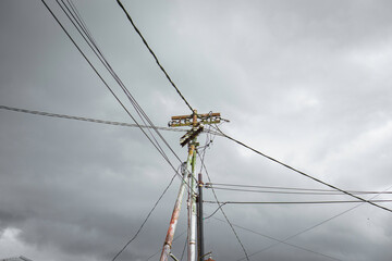 Fototapeta premium Messy utility power pole with tangled cables against a dramatic dark gray cloudy sky background - Tiang listrik dan kabel kusut