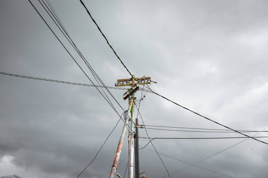 Messy utility power pole with tangled cables against a dramatic dark gray cloudy sky background - Tiang listrik dan kabel kusut