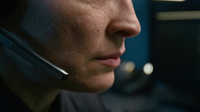 Side view close up shot of adult female dispatcher at police station and speaking to headset controlling operations with focus on lips moving, copy space