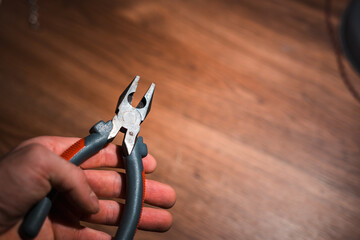 Hand holding pliers against a wooden background, tool close-up and copy space
