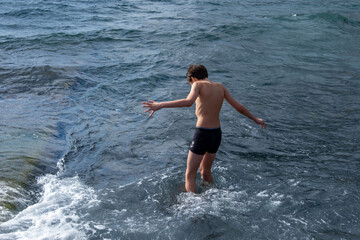Fototapeta premium Teen boy playing in ocean waves on black volcanic sand beach, joyful summer moment, natural fun, healthy childhood, barefoot freedom