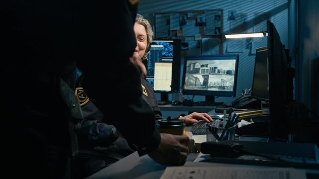 Side view shot of mature woman working as dispatcher at police station and wearing headset with colleague bringing food and coffee at night