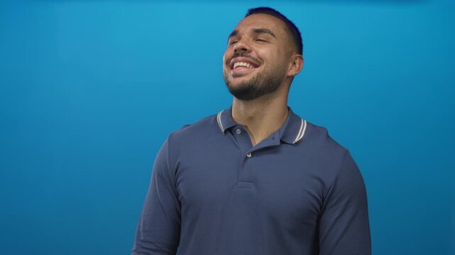 Man smiling with bare teeth in studio with upward gaze and open posture against blue backdrop; happiness.