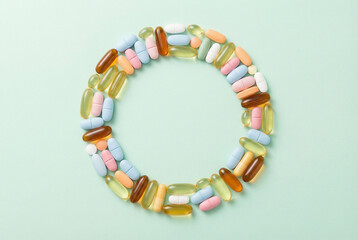 Colorful pills and capsules arranged in a circle on pastel mint background, healthcare and vitamins concept