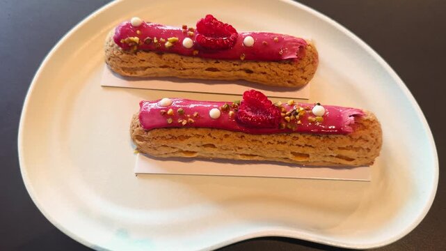 Fresh and delicious eclairs with sweet and sour raspberry cream, served on a white plate in a cozy French cafe.