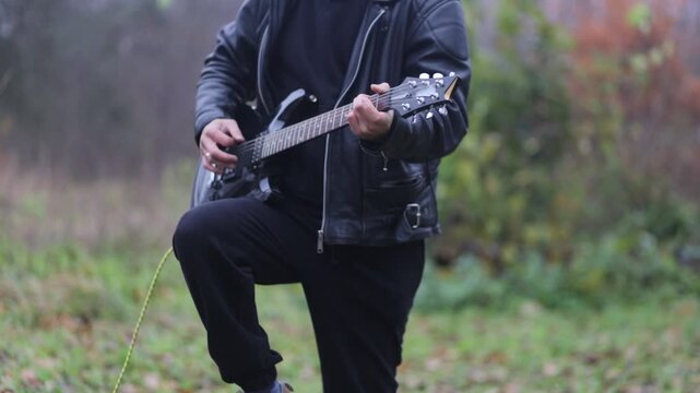 young female rock musician in a leather jacket plays an electric guitar outdoors