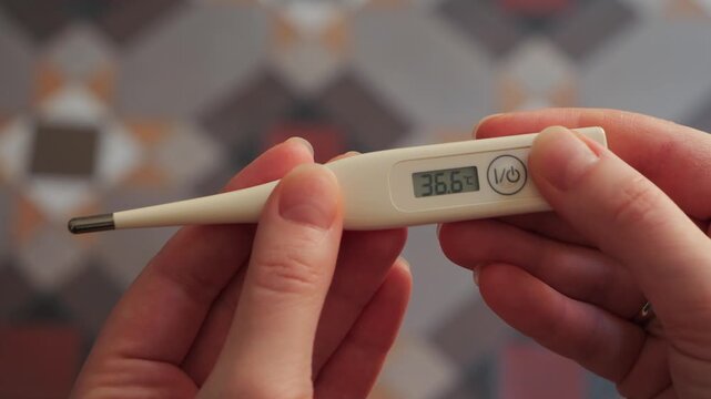 A hand holds a digital thermometer, and the screen displays a temperature of 36.6, which is considered a normal, healthy body temperature.