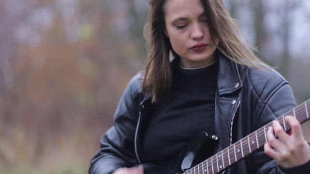Young woman in a leather jacket, rock musician plays electric guitar outdoors
