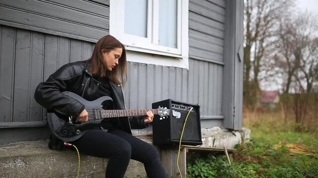 female rock musician in a leather jacket plays an electric guitar with an amplifier