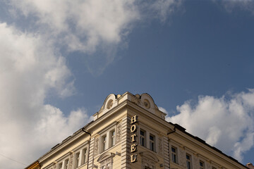 Ornate hotel corner with blue sky and billowing clouds, carved cornice and elegant signage, warm lateafternoon light © Alena
