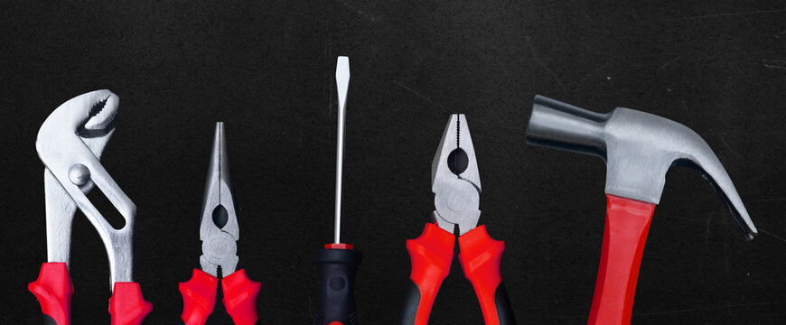 Set of basic hand tools including pliers screwdriver and hammer arranged on a dark background