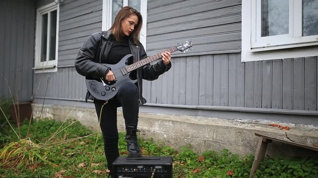 female rock musician in a leather jacket plays an electric guitar with an amplifier