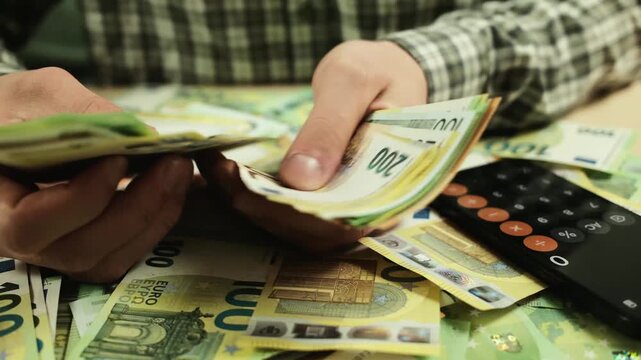 Hands counting euro banknotes on a table with scattered cash and a smartphone calculator. Concept of personal finance management, budgeting, saving money and financial planning