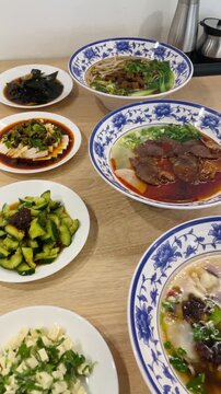 Vertical close-up of Chinese cuisine dishes arranged on a dining table. Several plates with prepared meals are placed together for serving. Cafe, bistro or restaurant or dining setting.