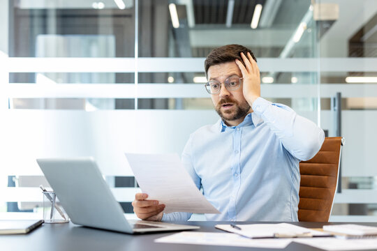 Businessman receiving stressful news while reviewing an official document, reacting with shock and worry about financial problems, debt, or an unforeseen crisis at work