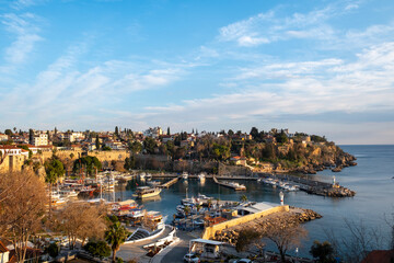 Naklejka premium Panoramic view of Kaleici marina and the historic old town of Antalya with boats in the harbor and warm golden hour sunset light illuminating the Mediterranean coastline in southern Türkiye.