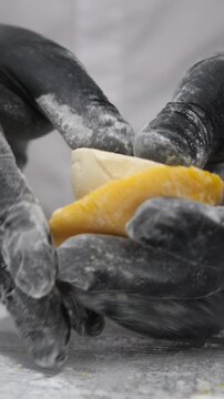 Vertical video. Confectioner in black gloves shapes tasty mango mochi with yellow rice dough in bakery closeup. Japanese chef hands cook delicious cakes with tropical fruits over countertop