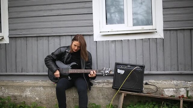 female rock musician in a leather jacket plays an electric guitar with an amplifier