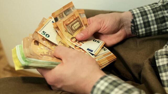 Hands counting a thick stack of euro banknotes while sitting indoors. Concept of cash income, financial management, budgeting and personal wealth