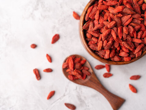 Dried Goji berries or Wolfberry scattered, vibrant red, in a wooden bowl on a textured background.