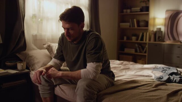 Middle aged man in pyjamas sitting on bed with trembling hands after sleepless night, stress and exhaustion catching up