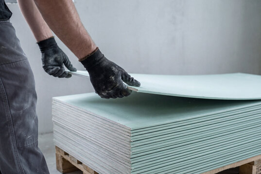 Construction worker lifting sheet of green moisture resistant drywall