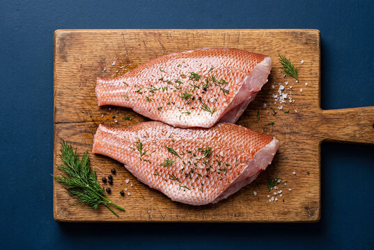 Raw red snapper fillets with herbs on wooden cutting board