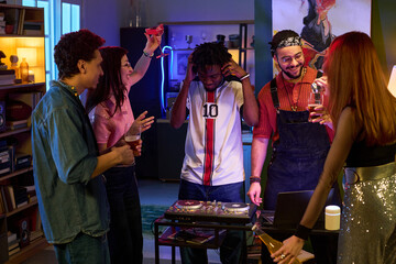 Group of multiethnic young people socializing around DJ turntable, Black man wearing headphones...