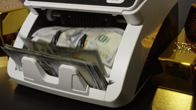 Money counting machine processing hundred dollar bills. Money count in motion. Gold bars and US dollars. Money counting action. Business concept with gold bar and money.