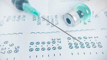 Medical syringe and vaccine vial over blood test results document, concept of vaccination, disease prevention and healthcare diagnostics
