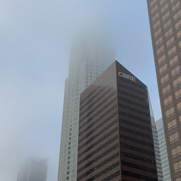 LOS ANGELES, CA, NOV 7, 2025: Street-level view of a brown CBRE-branded skyscraper in Downtown, dwarfed by a fog-swallowed glass skyscraper behind it