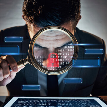 Close up of a man looking through a magnifying glass at binary code on a digital screen in a dark office setting
